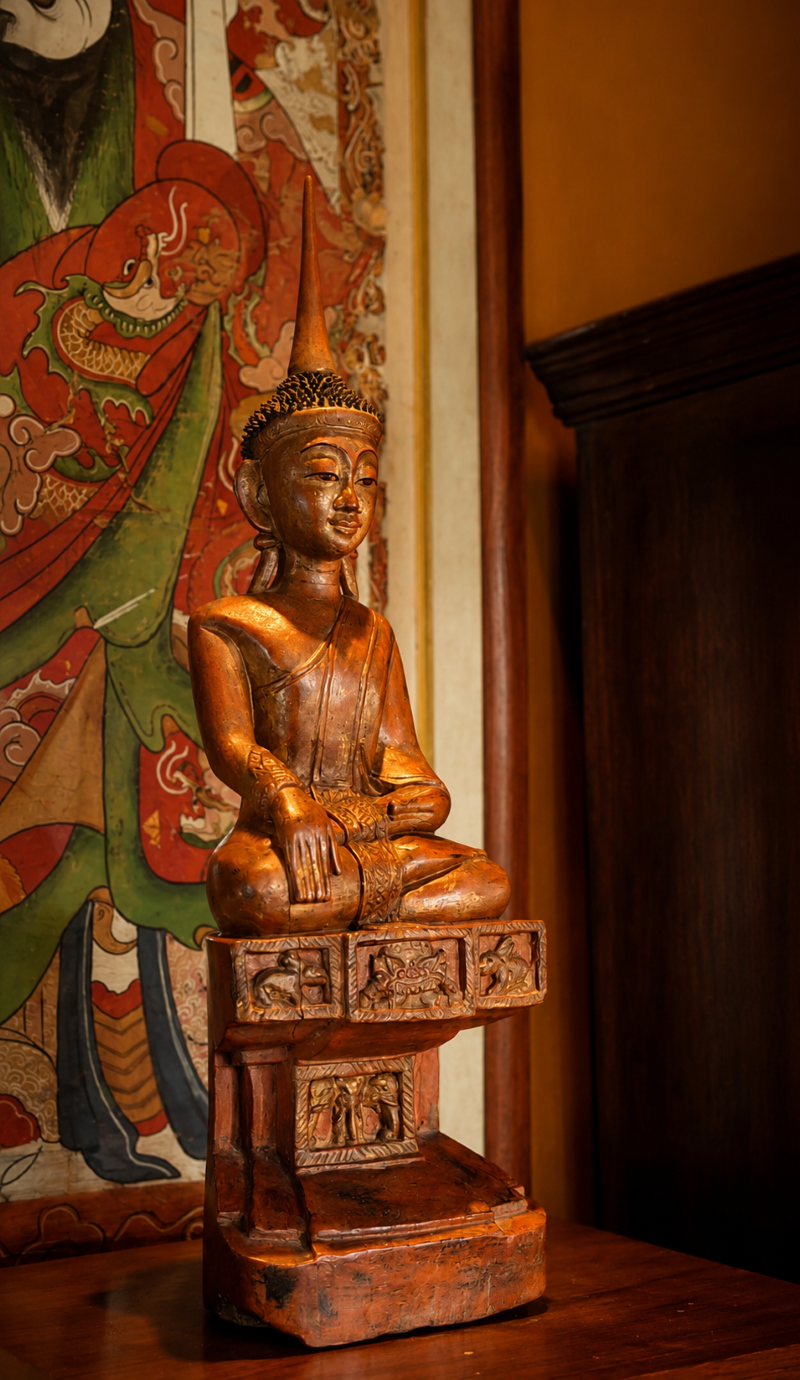 A carved wooden Buddha statue in the Bhumisparsha mudra (calling the earth to witness), featuring a gilded cone-shaped finial on top of its head, seated atop a decorative carved wooden throne
